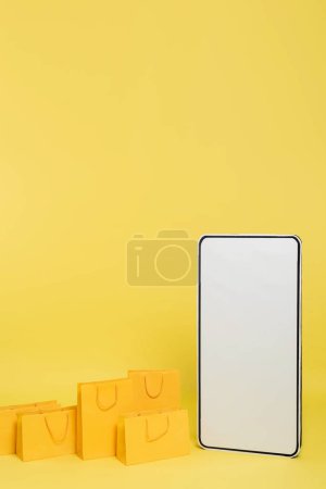 vertical view of shopping bags near huge smartphone template on yellow background