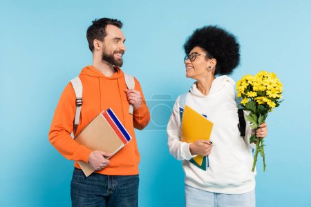 Photo for Happy african american student with flowers smiling at bearded boyfriend on blue - Royalty Free Image