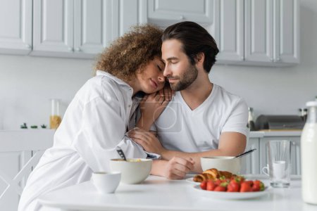 curly woman leaning on shoulder of bearded boyfriend during breakfast  