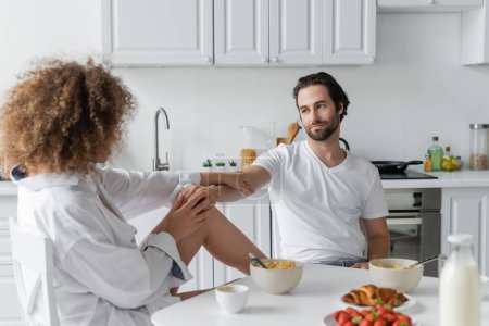curly woman seducing bearded boyfriend during breakfast in kitchen 