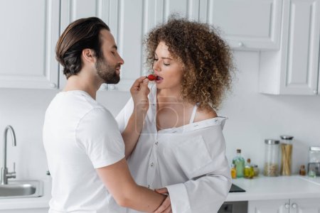 bearded man feeding curly and sexy girlfriend with fresh strawberry  