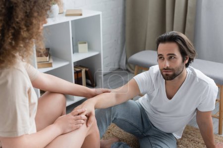 curly woman sitting and touching hand of bearded boyfriend in bedroom 