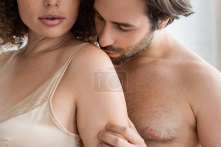 bearded and shirtless man kissing shoulder of sexy woman in silk night dress 