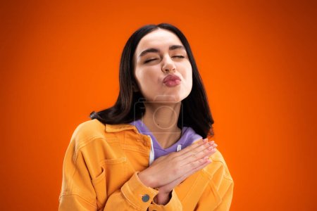 Photo for Young brunette woman pouting lips and closing eyes isolated on orange - Royalty Free Image