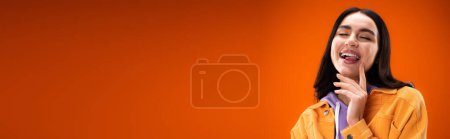 Photo for Young brunette woman sticking out tongue isolated on orange, banner - Royalty Free Image