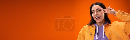 Téléchargez les photos : Positive young woman showing victory sign isolated on orange, banner - en image libre de droit