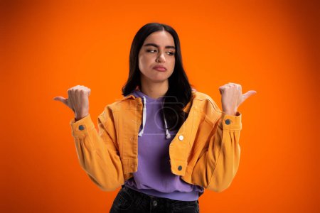 Photo for Skeptical brunette woman pointing with fingers isolated on orange - Royalty Free Image