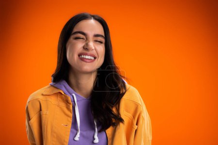Photo for Happy young woman in jacket closing eyes isolated on orange - Royalty Free Image