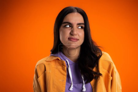 Offended brunette woman looking away isolated on orange