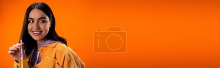 Pretty brunette woman holding juice with dinking straw isolated on orange, banner 