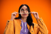 Young woman holding bamboo chopsticks near mouth and pouting lips isolated on orange Longsleeve T-shirt #635935356