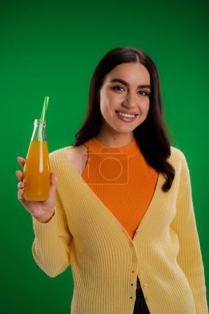 Téléchargez les photos : Happy brunette woman holding bottle of fresh juice with straw isolated on green - en image libre de droit