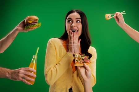 Photo for Astonished woman covering mouth with hands near people proposing different food isolated on green - Royalty Free Image