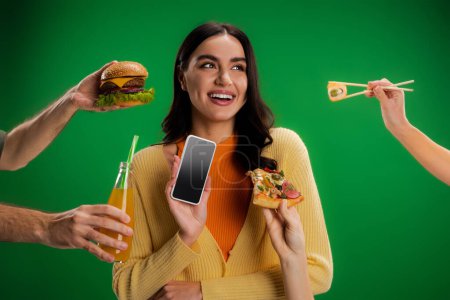Photo for Happy woman holding smartphone with blank screen near people with assortment of food isolated on green - Royalty Free Image