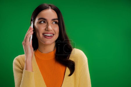Téléchargez les photos : Young and happy woman in stylish clothes talking on mobile phone isolated on green - en image libre de droit