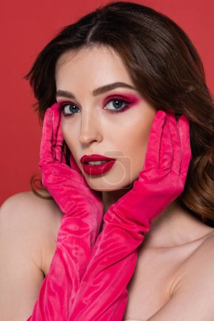 portrait of young woman with magenta color eye shadow looking at camera isolated on pink 