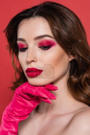 portrait of pretty young woman with magenta color eye shadow posing isolated on pink 