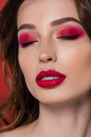 Téléchargez les photos : Close up of young woman with closed eyes and magenta color eye shadow isolated on pink - en image libre de droit
