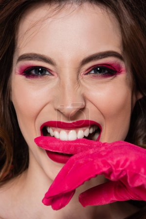 portrait of young woman with makeup biting magenta color glove 