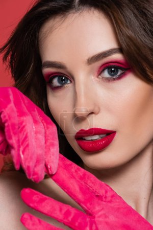 portrait of young woman with magenta color eye shadow pulling glove isolated on pink 