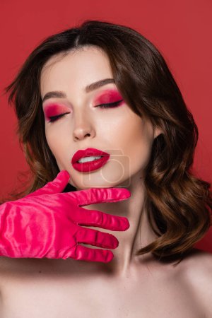 young woman with magenta color eye shadow posing with closed eyes isolated on pink 