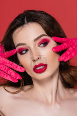 Foto de Portrait of young woman with magenta color eye makeup posing in bright gloves isolated on pink - Imagen libre de derechos