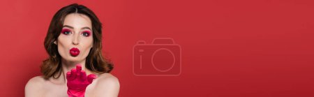 Foto de Portrait of young woman with magenta color eye makeup sending air kiss isolated on pink, banner - Imagen libre de derechos
