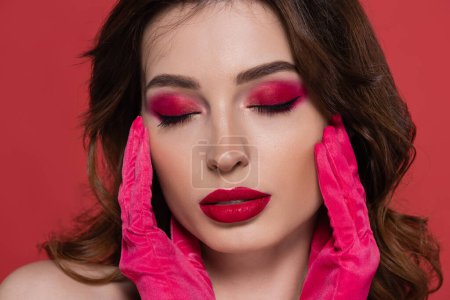portrait of brunette woman with magenta color makeup and closed eyes isolated on pink 