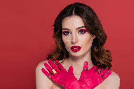 Téléchargez les photos : Portrait of young woman with magenta color gloves and golden rings posing with crossed arms isolated on pink - en image libre de droit