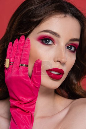 portrait of young woman with magenta color makeup and glove with golden rings isolated on pink 
