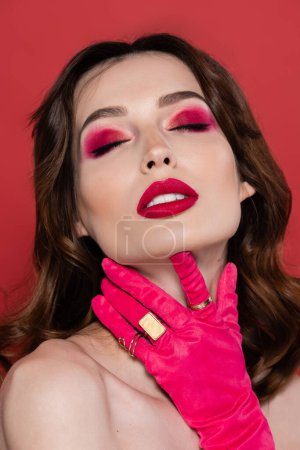 portrait of young woman with magenta color glove with golden rings touching neck isolated on pink 
