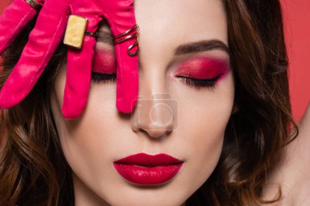 close up of woman in magenta color glove with golden rings covering closed eye isolated on pink 