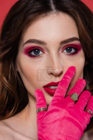 close up of young woman with magenta color makeup and glove isolated on pink 