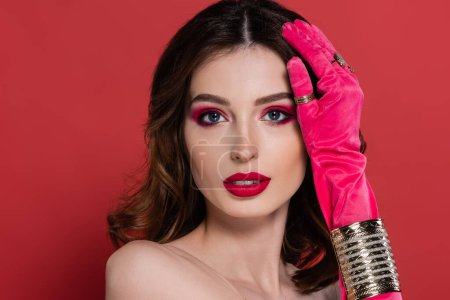 portrait of young woman in magenta color glove with golden rings and bracelet posing isolated on pink 