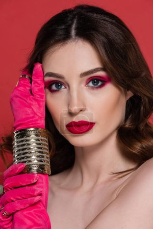 Foto de Portrait of young woman in magenta color gloves with golden rings and bracelet posing isolated on pink - Imagen libre de derechos