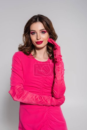 Photo for Cheerful young woman in magenta color gloves and dress isolated on grey - Royalty Free Image