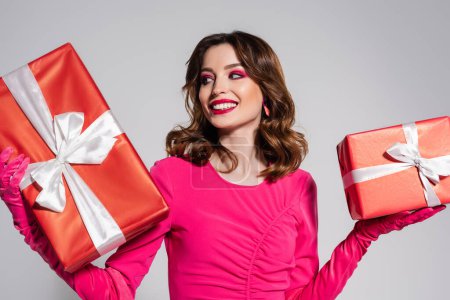 Téléchargez les photos : Happy young woman in magenta color dress and gloves holding presents isolated on grey - en image libre de droit