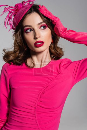 Téléchargez les photos : Pretty young woman in magenta color glove and hat with feather posing isolated on grey - en image libre de droit