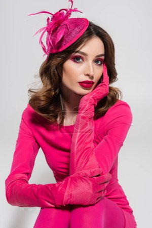 portrait of young brunette woman in elegant hat and magenta color gloves isolated on grey 