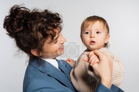 Téléchargez les photos : Happy mother in blue suit holding surprised toddler girl in sweater isolated on grey - en image libre de droit