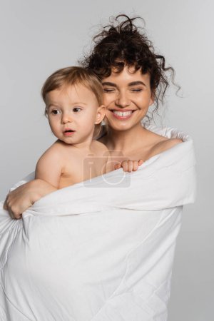 happy mother and toddler baby girl covered in duvet isolated on grey 
