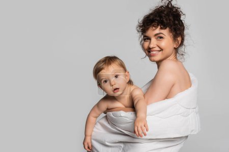 joyful mother and toddler baby girl covered in duvet isolated on grey 