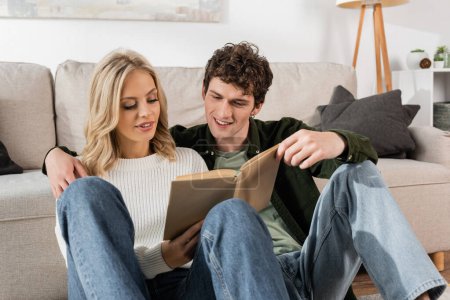 young couple smiling while reading book together in living room 