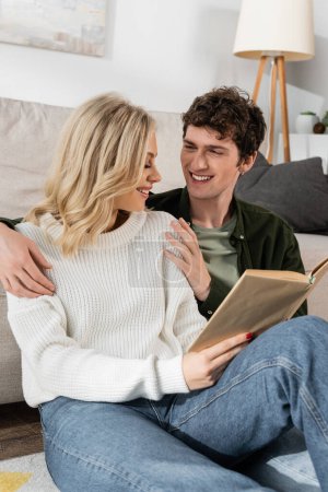 happy couple smiling while reading book together in living room 