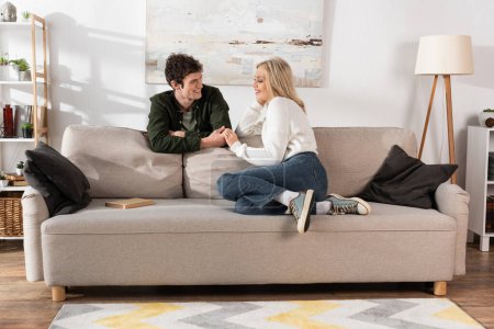 full length of young woman with blonde hair looking at curly boyfriend in living room 