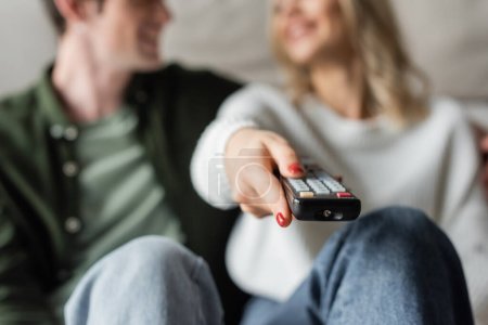 Foto de Cropped view of woman clicking channels with remote controller near boyfriend on blurred background - Imagen libre de derechos
