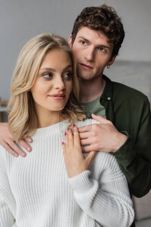 portrait of curly young man hugging blonde woman in white sweater 