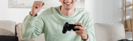 Photo for KYIV, UKRAINE - OCTOBER 24, 2022: cropped view of excited young man in sweatshirt playing video game, banner - Royalty Free Image
