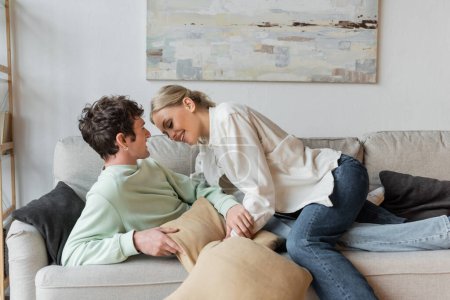 Foto de Happy young couple laughing while holding pillows in living room - Imagen libre de derechos
