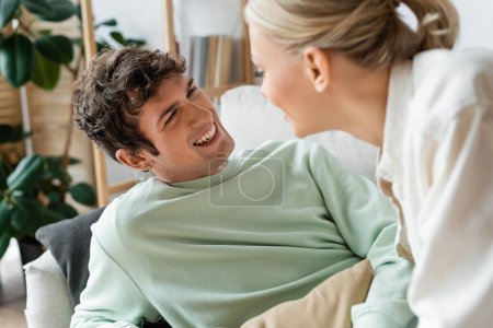 cheerful young man laughing while looking at girlfriend on blurred foreground 
